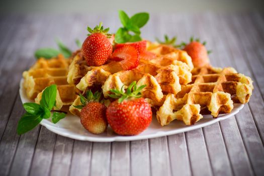 Sweet curd cooked waffles with fresh ripe strawberries, on a wooden table.