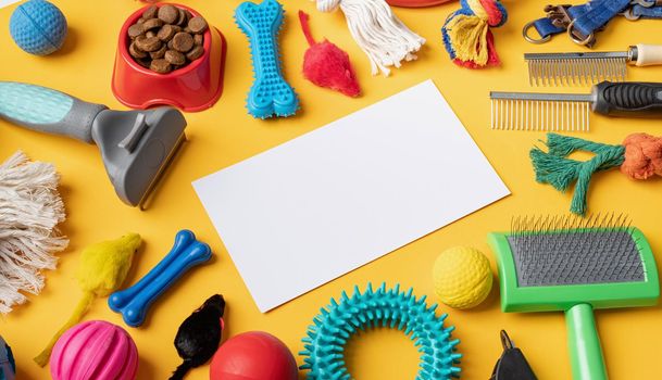 Pet care concept, various pet accessories and tools, toys, balls, brushes on yellow background with blank paper for mockup design,high angle