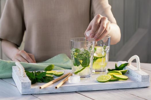 Girl prepares summer refreshing mojito fruit cocktails with lime and mint.