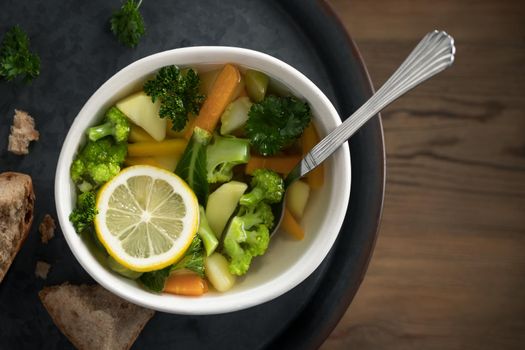 Vegetarian vegetable soup with carrots, broccoli and parsley in a light bowl on a metal tray on a wooden table.