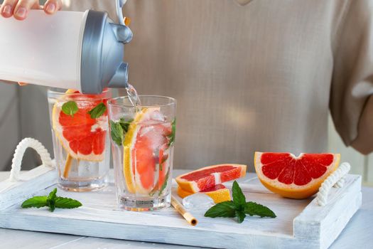 Girl cooking summer refreshing fruit cocktail with grapefruit slices and mint.