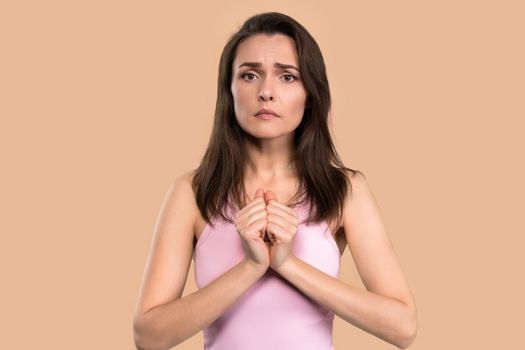 Asking help or praying worried woman with hands put together looking in camera with help need in her eyes. Hopeful religious woman in hope for forgiveness isolated on beige background.