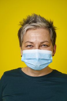 Happy eyes smiling grey short haired doctor woman wearing medical face mask looking at camera wearing green blouse isolated on yellow background.