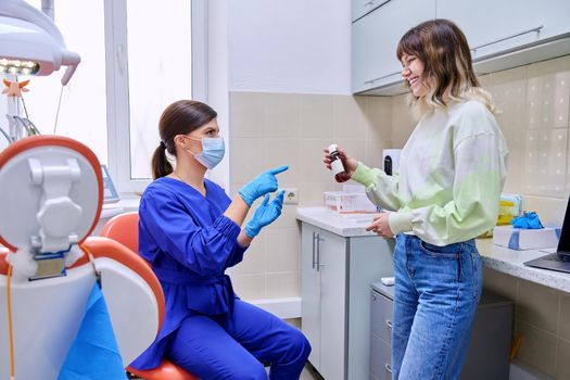 Dentist doctor showing telling giving medicine for teeth and oral cavity in bottle to young teenage female in office. Dentistry, health care, treatment, people, medicine concept