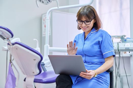 Online consultation, nurse help in clinic using laptop. Female doctor dentistwaving hand talkingtalking looking in laptop in dental office. Video conference, videocall, service, dentistry, medicine concept