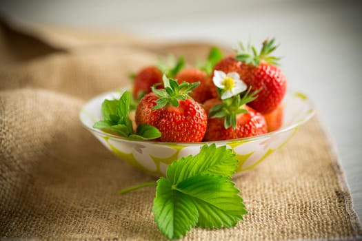 ripe red strawberries in a bowl on a burlap tablecloth, on a wooden table