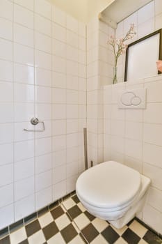 Interior of narrow restroom with sink and wall hung toilet with white walls and checkered floor