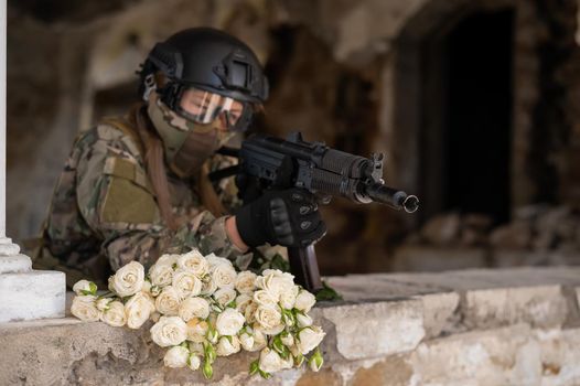 Caucasian woman in military uniform holding a machine gun and a bouquet of white roses