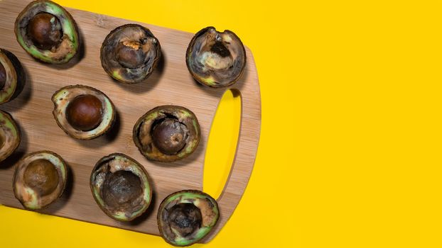 Rotten Avocado halves on Yellow Background. Food Fruits cannot be eaten. Overripe avocado fruit cuts in halfs. Stop wasting food. Unhelthy bad food Concept. Copy Space.