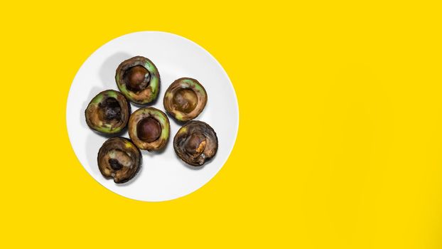 Bad Avocado halfs on Yellow background. Rotten Food Contaminated Avocado Necomestibile Fruits Wasting Food Unhealthy Tropical Fruits. Food concept Copy space.