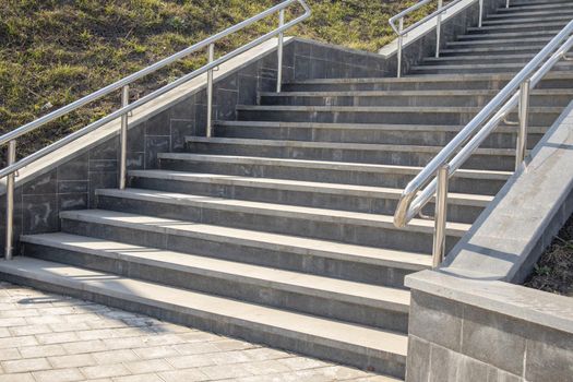 Outdoor concrete steps on a modern city staircase with metal railings on a sunny day, outdoors, bottom view.