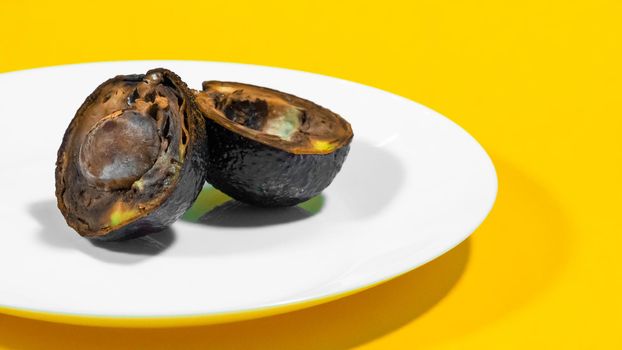 An avocado cut in half moldy on a plate Yellow background Rotten Food Contaminated Avocado Necomestibile Fruits Wasting Food Unhealthy Tropical Fruits. Food Concept. Copy space.