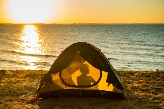 Woman and dog in a tourist tent at sunset. Camping with a pet.