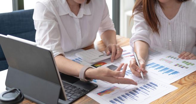 Two women analyzing documents while sitting on a table in office. Woman executives at work in office discussing some paperwork..