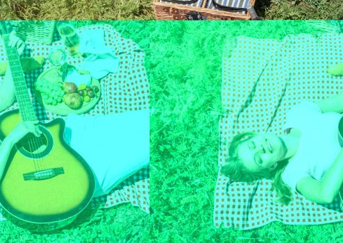 Top view of young caucasian woman in white pants outside having picnic, eating and playing guitar. Summer fun and leisure