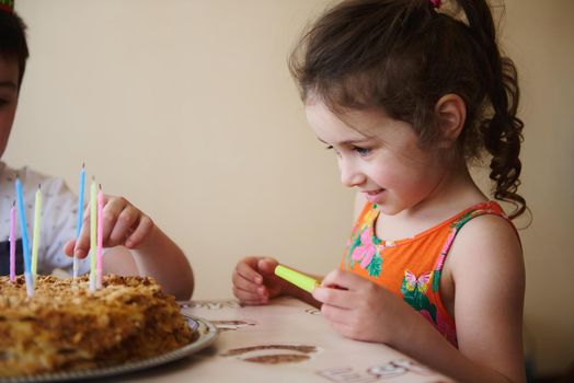 Close up portrait of a happy smiling adorable child, 5 year old Caucasian girl standing at the table with a birthday cake. Celebration, anniversary event concept