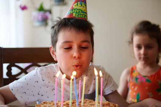 Adorable Caucasian boy blowing candles on his birthday cake, celebrating his 10th year anniversary at home. Birthday party concept.