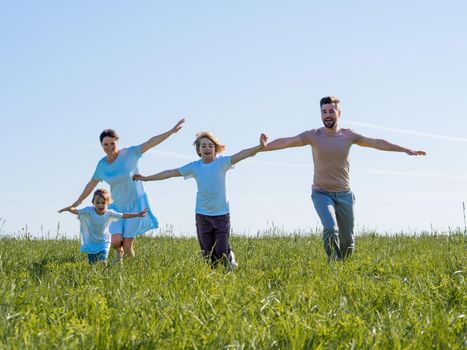 Excited happy family running on green grass meadow