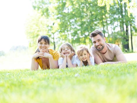 Family of four laying on green grass in summer park
