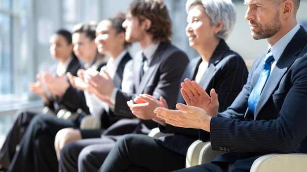 Business people sitting in a row and applauding at conference