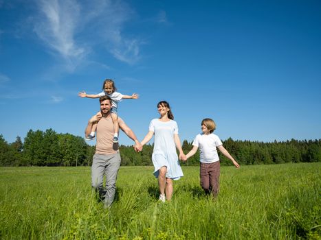 Happy family of parents and two children walking on summer grass meadow