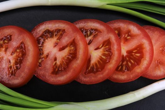 Tomato slices in a frame of green onions close-up on a black background. The concept of healthy eating..