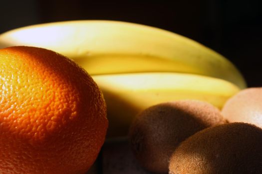 Kiwi, bananas, orange under the falling light from the window on a black background..