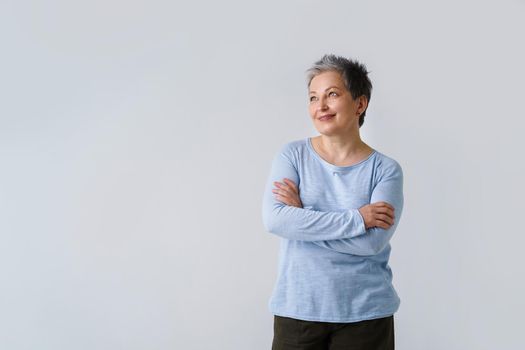 Happy mature grey hair woman posing with hands folded looking sideways up, copy space on left isolated on white background. Healthcare concept. Aged beauty concept.