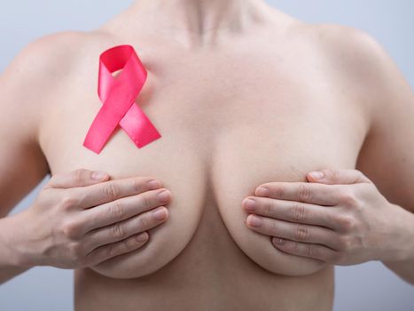 Pink breast cancer awareness ribbon on the chest of a naked woman on a white background