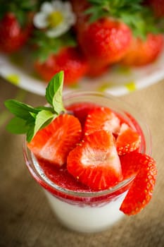 sweet homemade yogurt with strawberry jam and fresh strawberries in a glass cup, on a wooden table.