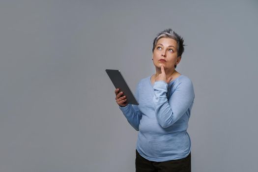 Marvelous mature woman 50s grey haired with digital tablet working or checking on social media. Pretty woman in blue blouse isolated on white. Older people and technologies. Toned image.