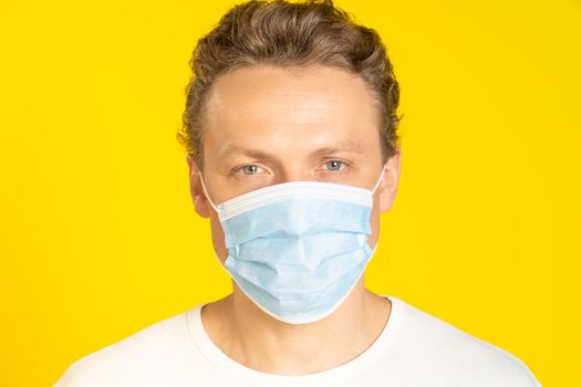 Handsome blond man wearing medical face mask prevention pandemic coronavirus or monkeypox. Handsome man in white t-shirt and medical mask on yellow background. Panoramic, healthcare concept.