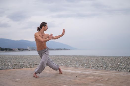 Caucasian man with naked torso practicing wushu on the seashore