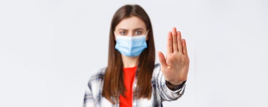 Coronavirus outbreak, leisure on quarantine, social distancing and emotions concept. Close-up of serious woman stretch palm to say stop, restrict or prohibit from bad decisions, wear medical mask.