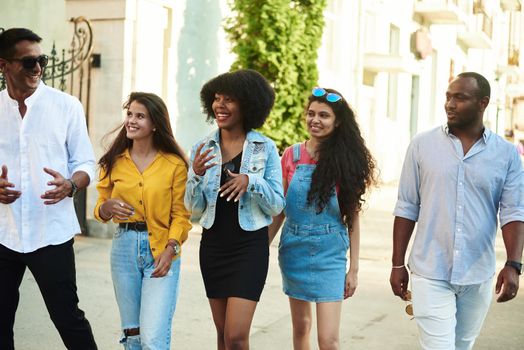 College students walking together outdoors. Young beautiful people of different nationalities walk around the city and talk.