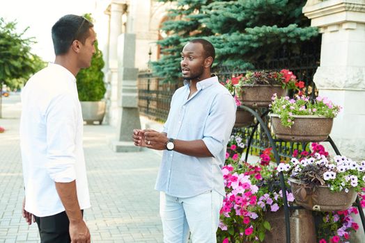 A black businessman is talking in an informal setting with a business partner on a city street.