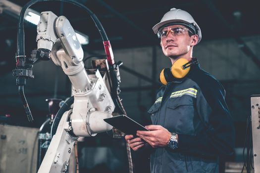 Young factory worker working with adept robotic arm in a workshop . Industry robot programming software for automated manufacturing technology .