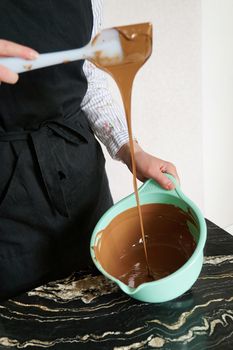 Close photo - confectioner - woman stirs chocolate for making homemade chocolates. Candy making, pastry production, bakery, dessert concept