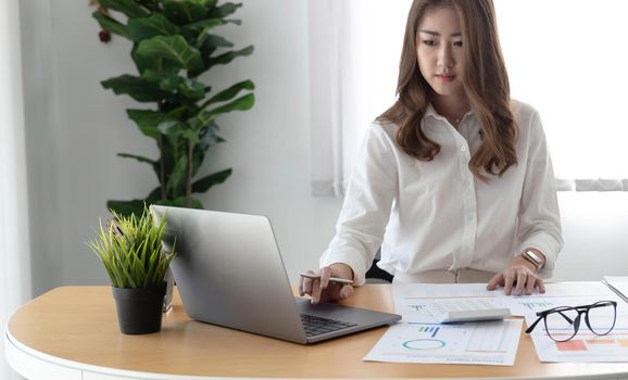 Young Asian businesswoman is happy to work at the modern office using a laptop computer..