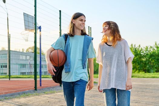 Young teenage male female students with backpacks ball walking outdoor near basketball playground court. Youth, active healthy lifestyle, education, college, high school, urban sport concept