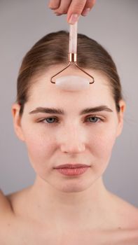 Close-up portrait of a woman uses a quartz roller massager to smooth wrinkles on her forehead