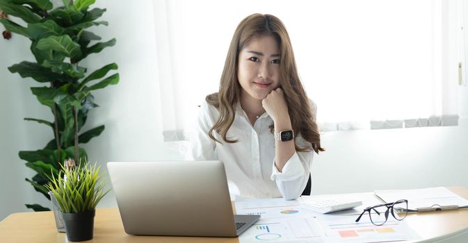 Charming Asian woman working at the office using a laptop Looking at the camera..