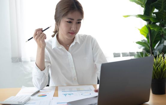 Asian businesswoman analyzes charts using laptop calculator at the office