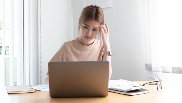 Young Asian woman feeling migraine head strain. Tired, Overworked businesswoman financier while working on laptop computer in office..