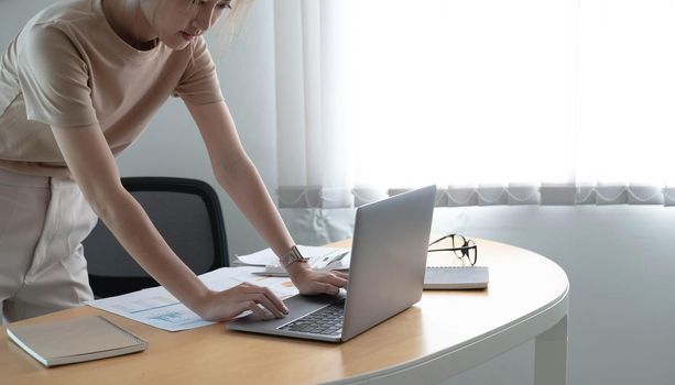 Attractive young brunette asian woman using laptop computer while standing in a stylish office room