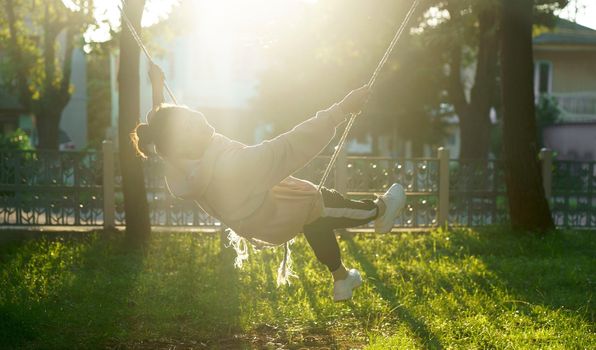 a woman rides on a swing near her house on a sunny day.