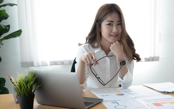 Charming Asian woman working at the office using a laptop Looking at the camera..