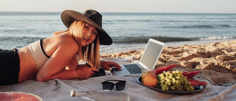 Side View of Cheerful Woman Dressed in Swimsuit Smiling to the Camera, Working on Digital Tablet and Laptop During Picnic by Sea
