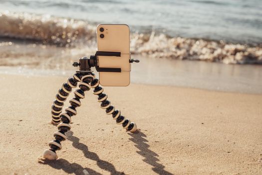 Smartphone Attached to Tripod Standing on Sandy Beach by Sea