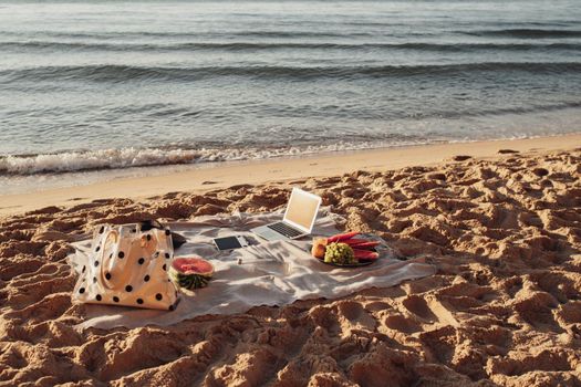 Picnic Set by the Sea, Laptop with Tablet and Fruits Lying on Plaid on the Sandy Beach